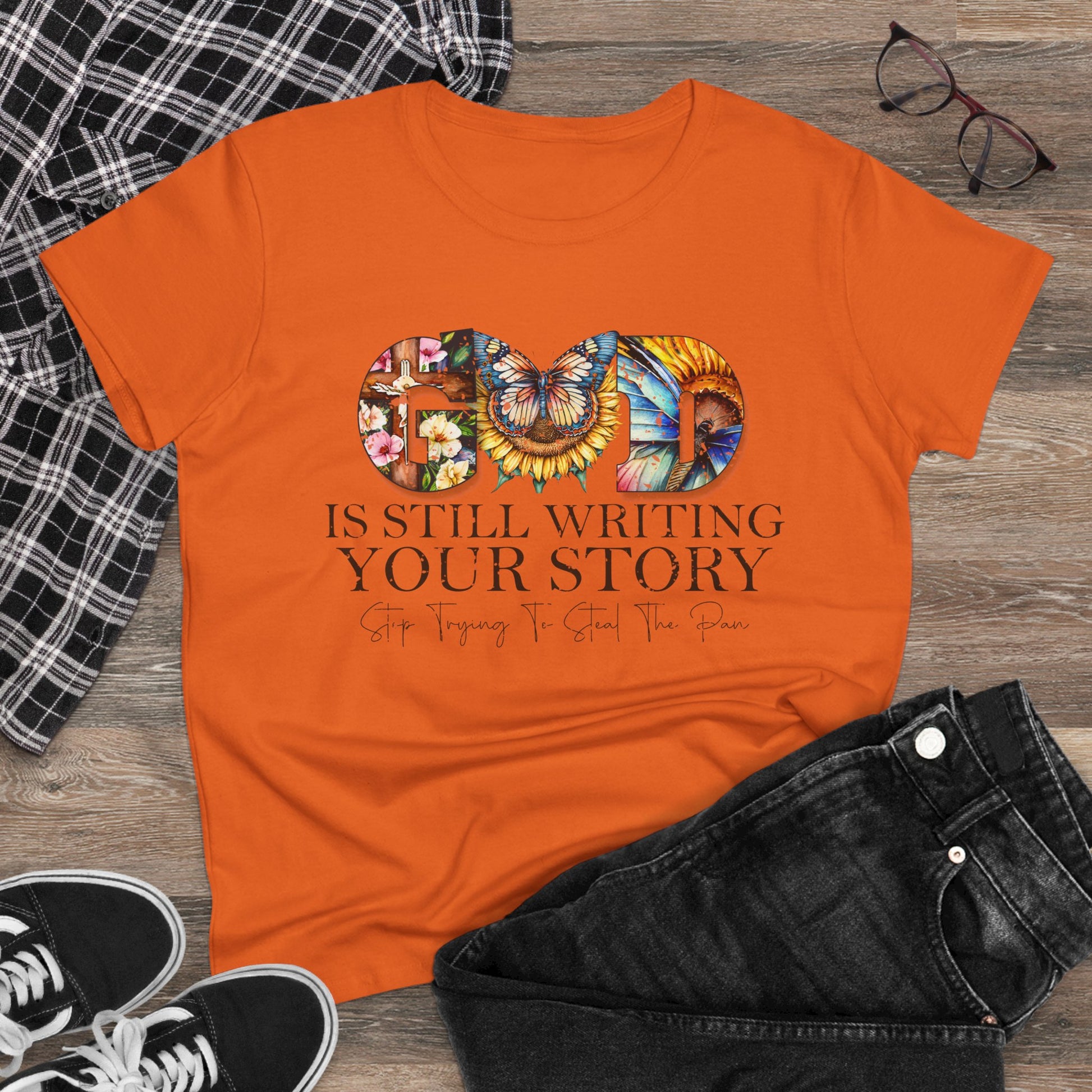 Orange t-shirt with colorful design and text on a wooden surface with casual items.