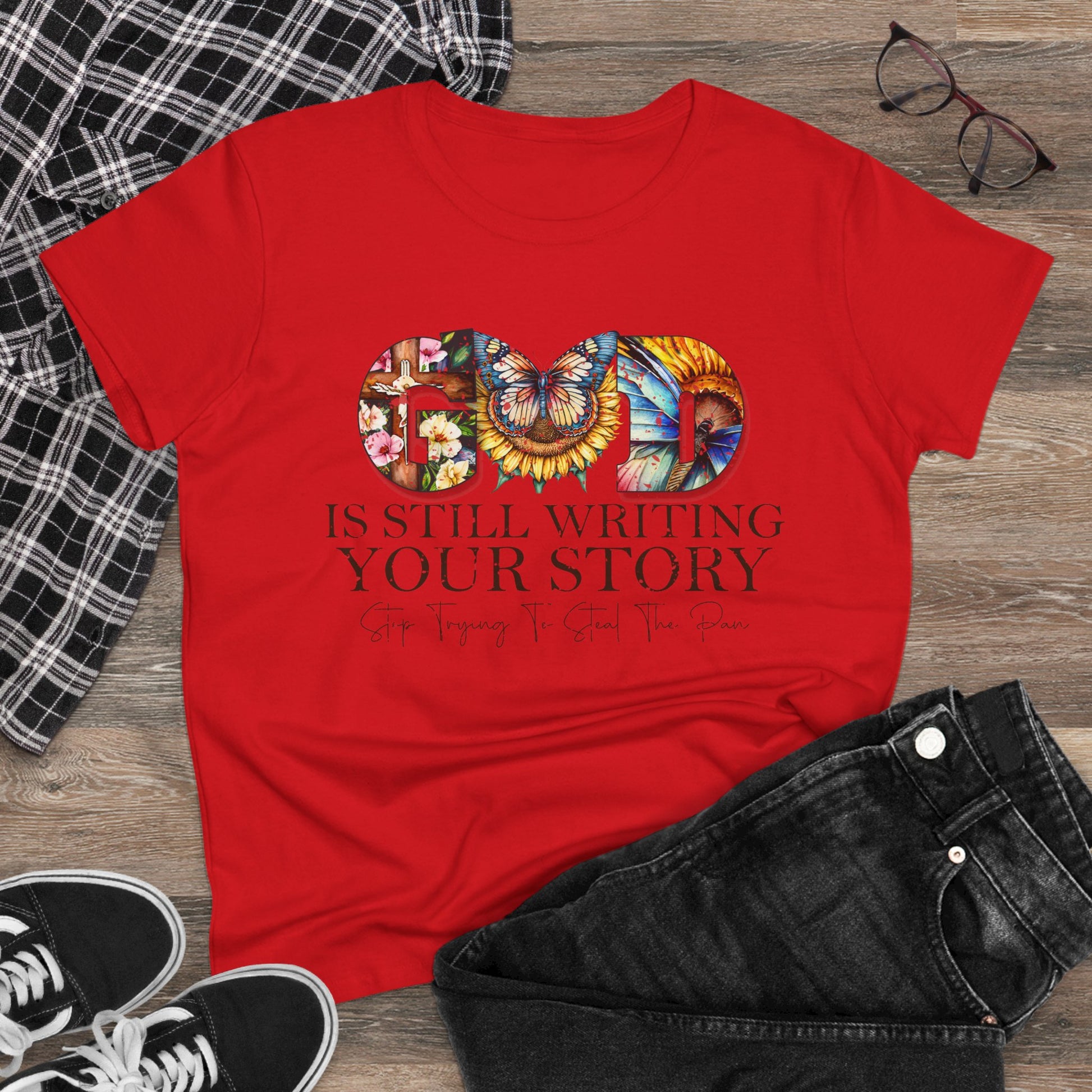 Red t-shirt with colorful graphic and text on a wooden surface with casual items.